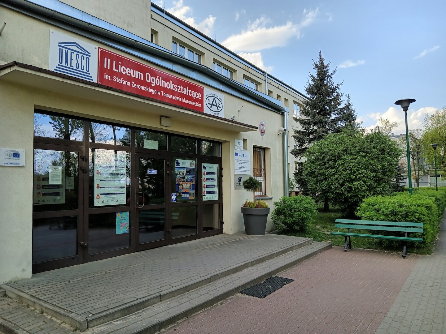 Zweistöckiger Schuleingang mit Glastüren und einer Holzbank.