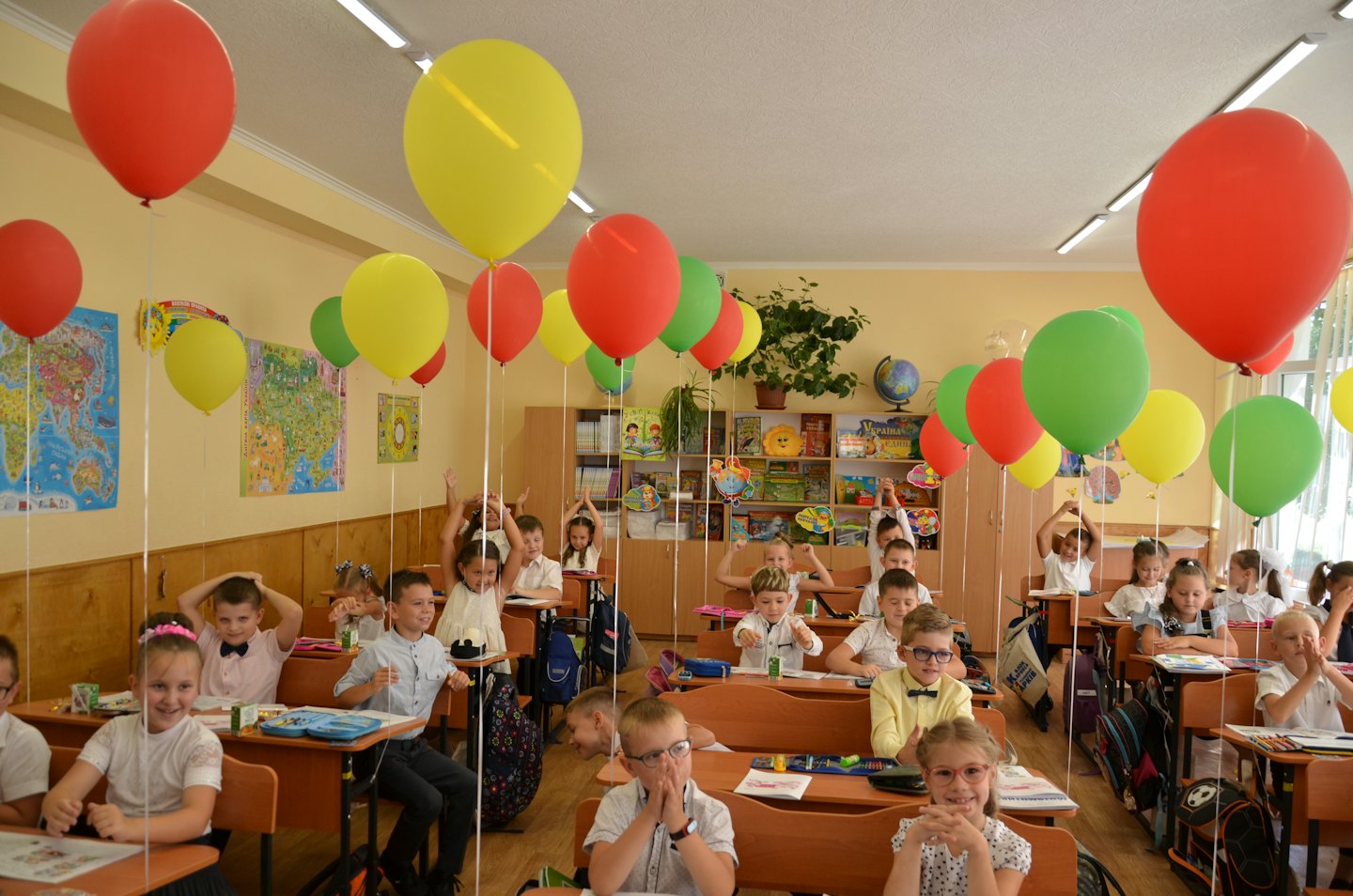 Schüler sitzen an Schreibtischen in einem Klassenzimmer voller Ballons.