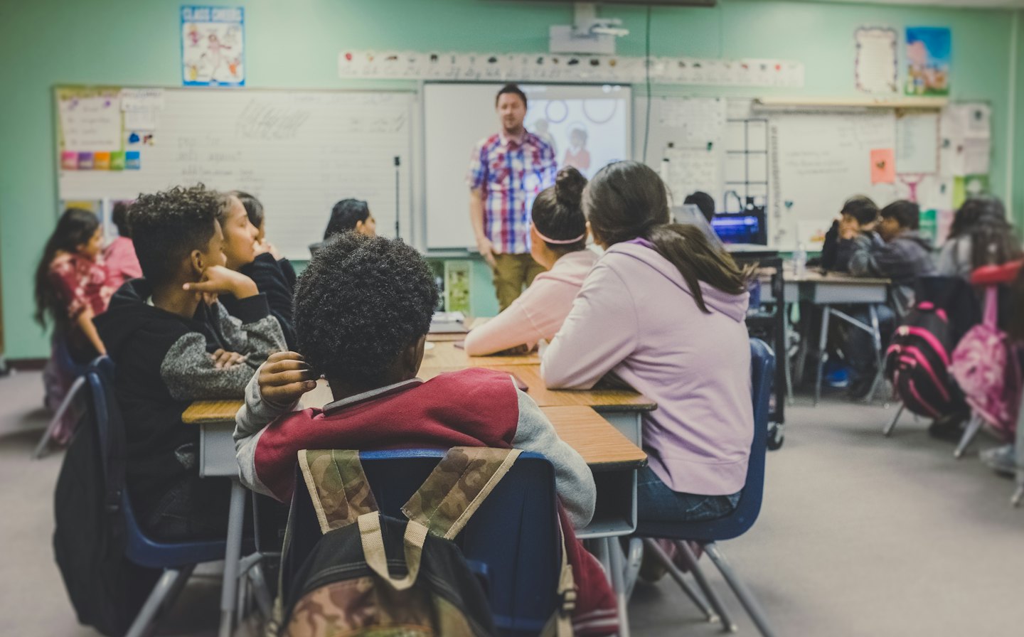 Schülerinnen und Schüler, die im Unterricht aufmerksam einer Lehrerin zuhören.